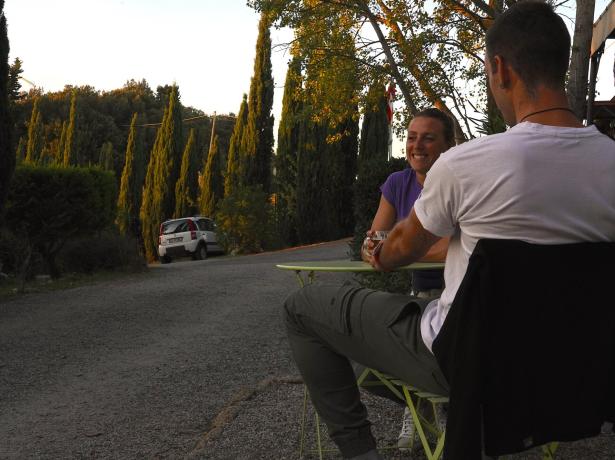 Two people chatting outdoors near a tree-lined road.