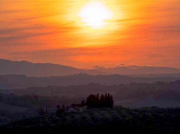 Breathtaking sunset over rolling hills with houses and trees.