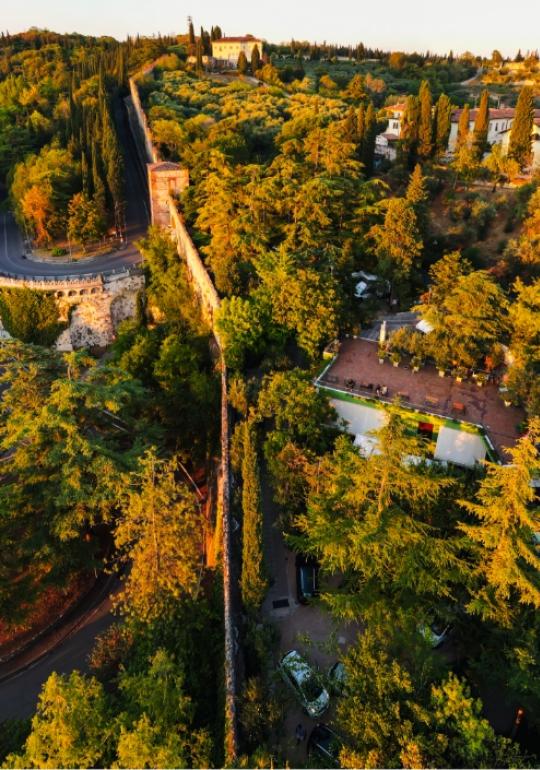 Sunset over hilly landscape, trees, and ancient walls.
