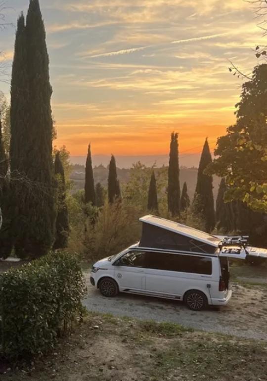Camper al tramonto tra cipressi, atmosfera serena e calda.