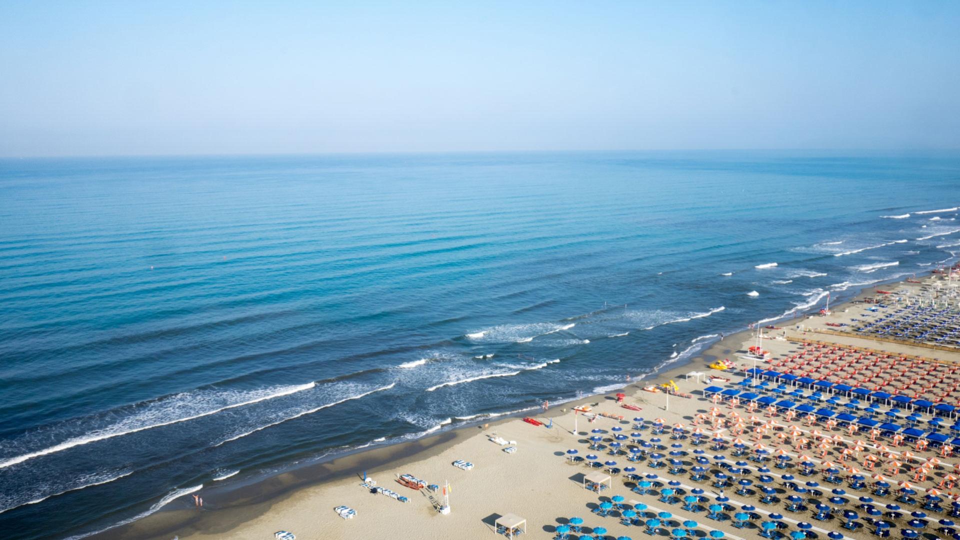 Strand mit bunten Sonnenschirmen und ruhigem Meer.