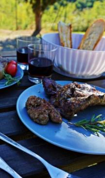 Outdoor dinner with grilled meat, bread, and red wine.