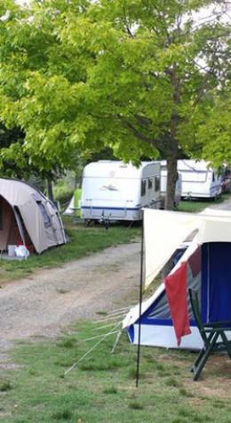 Camping site with caravans and tents under green trees.