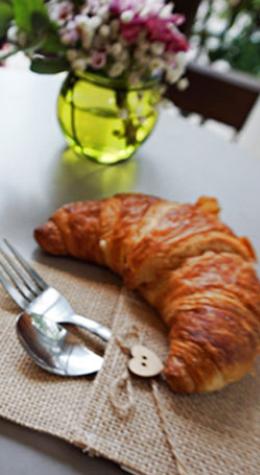Croissant on table with cutlery and flower vase.